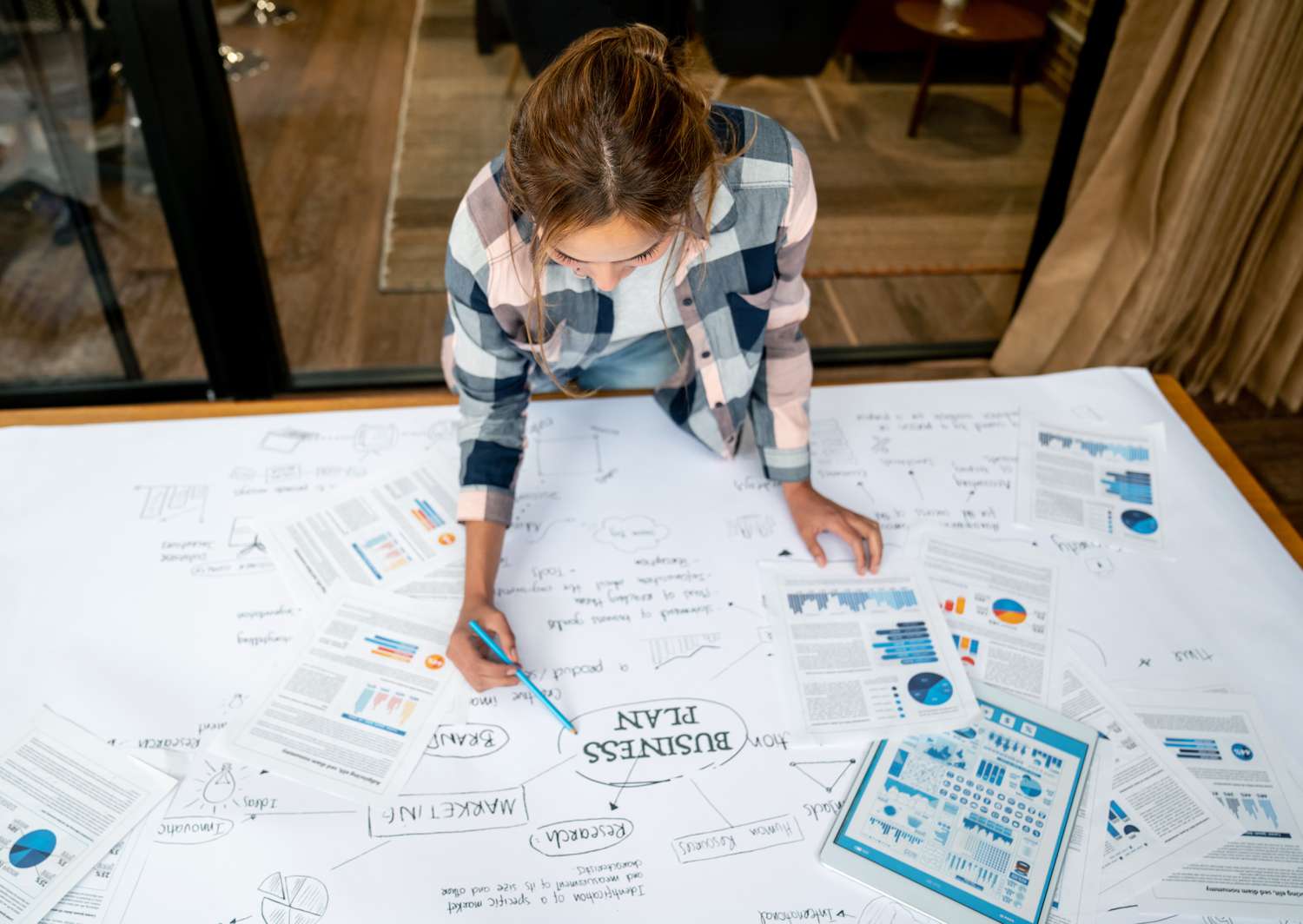 woman at a large table with multiple papers spread out on a table putting together a business plan