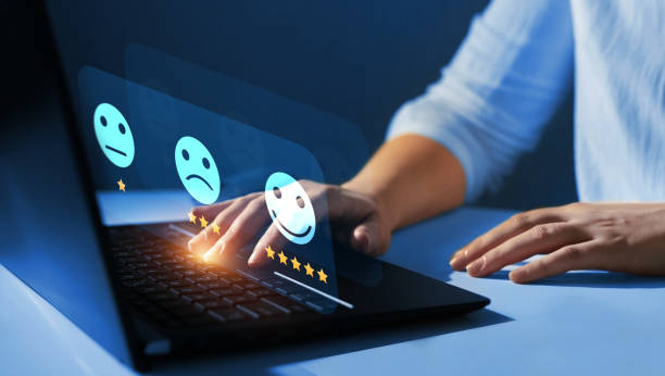 person at a computer with a close up of their hands and a laptop with a rating scale with smiley faces.