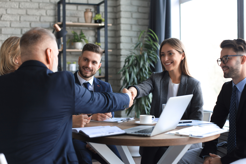 Business professionals shaking hands during a meeting, finalizing plans for data analysis service implementation.