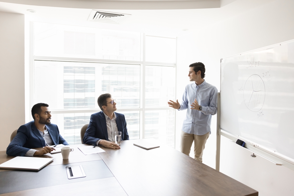Businessman presenting to colleagues in a meeting room, showcasing a pitch deck for startup funding and strategy alignment.