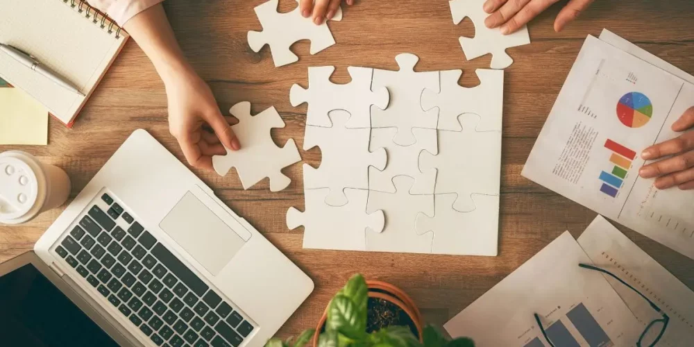 Business consultant assembling puzzle pieces on a desk with charts, laptop, and reports — symbolizing strategy and digital planning.
