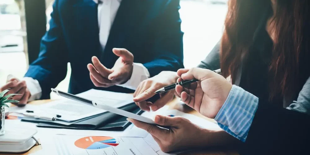 Close-up of business professionals engaged in a consulting services strategy meeting, analyzing data charts and discussing corporate growth plans.